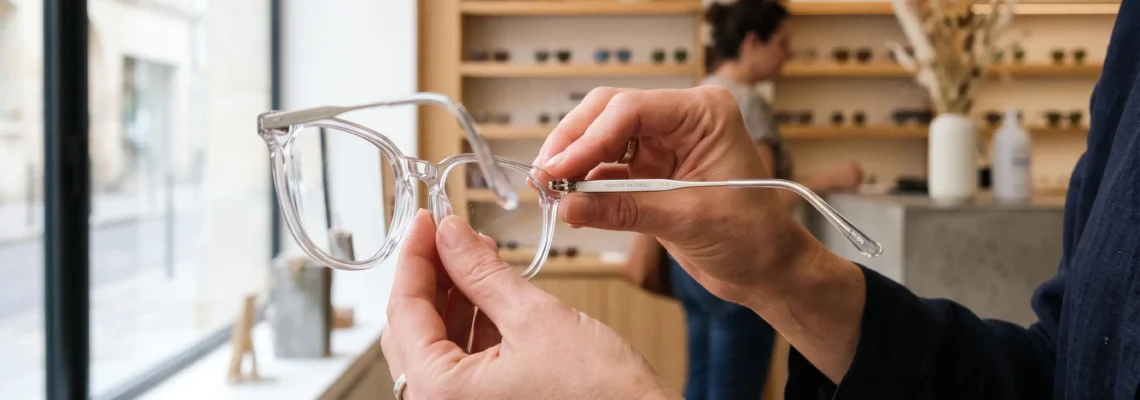 Un opticien présente une monture transparente associant acétate clair et métal.